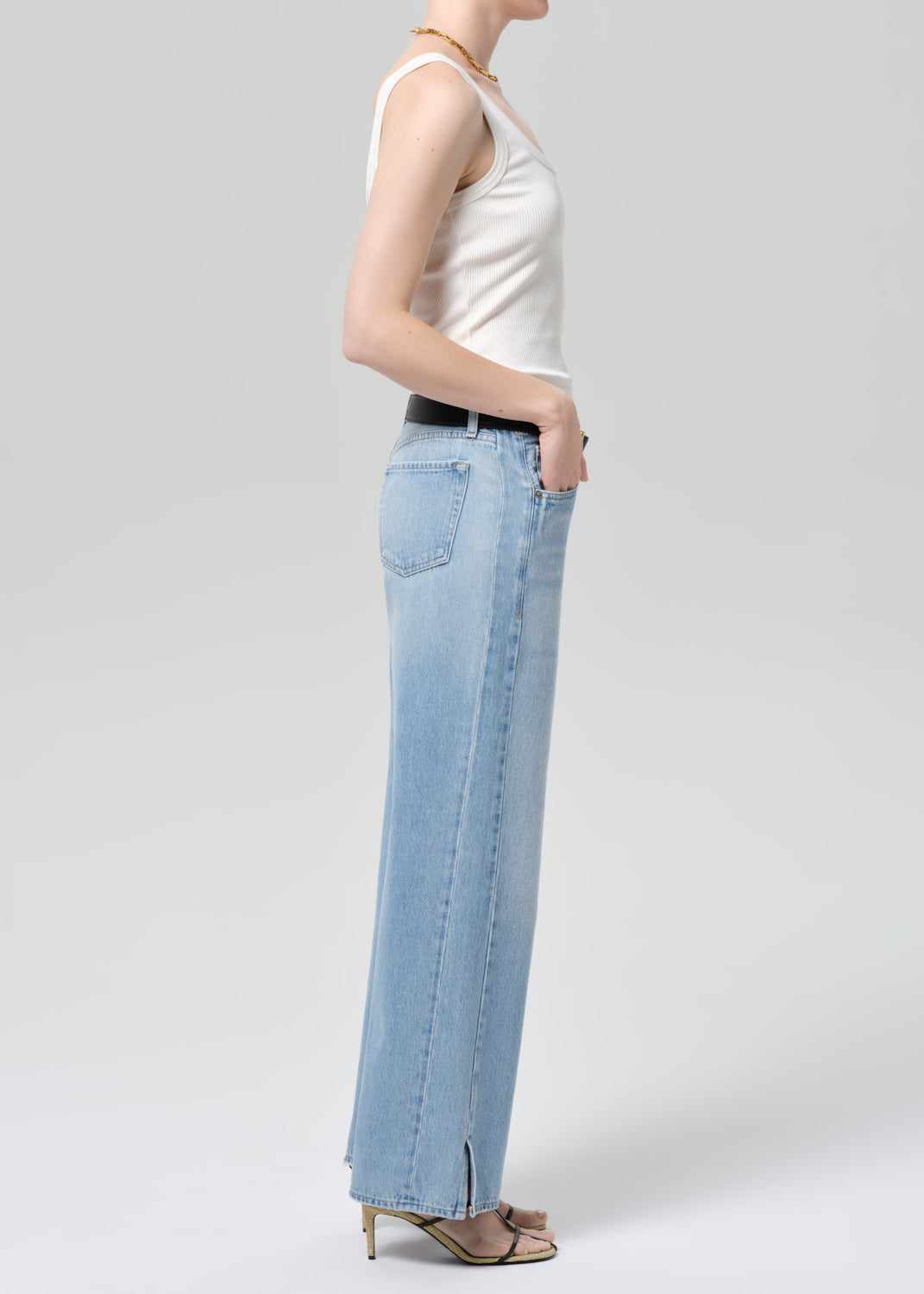 Person wearing light blue jeans and a white top on a plain background