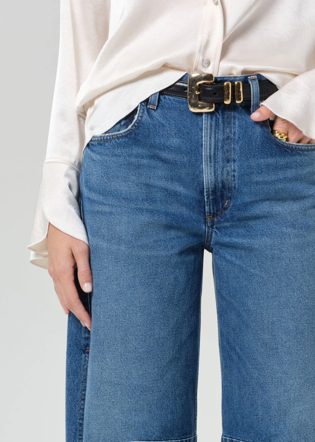 Person wearing blue jeans with a white shirt on a plain background