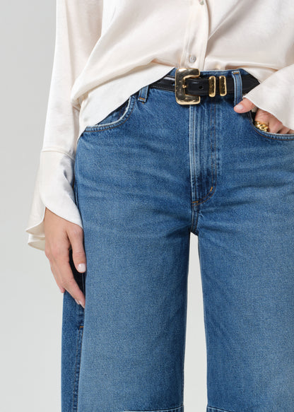 Person wearing blue jeans with a white shirt on a plain background