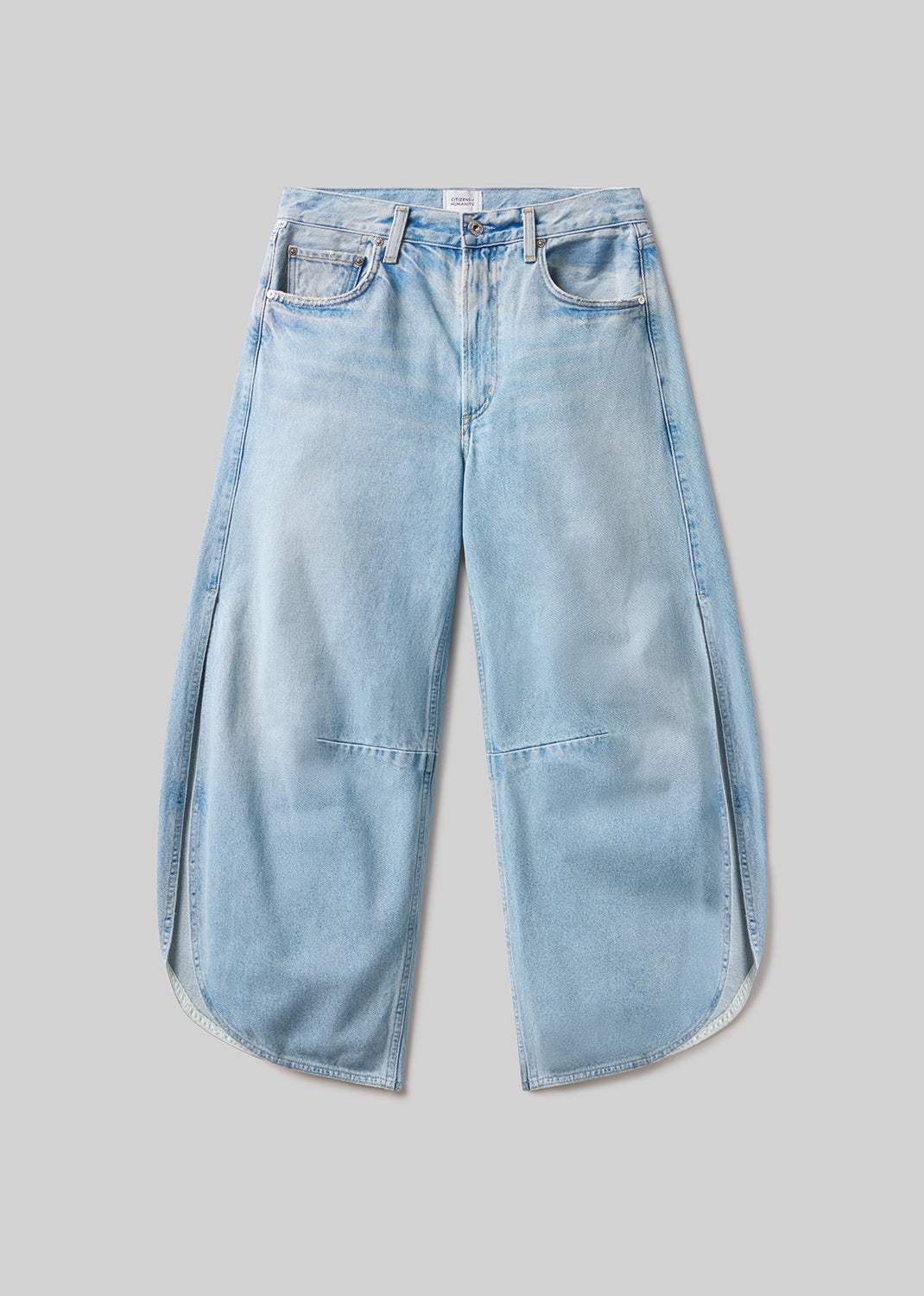 Light blue wash wide-leg denim jeans with a five-pocket design, curved side seams, overlapping panel details, and rounded hems, front flat lay view on a grey background.