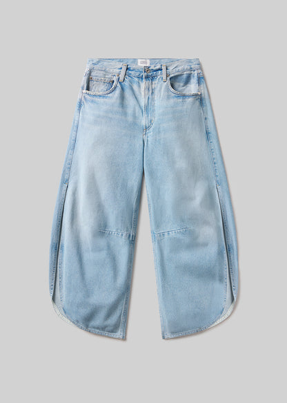 Light blue wash wide-leg denim jeans with a five-pocket design, curved side seams, overlapping panel details, and rounded hems, front flat lay view on a grey background.