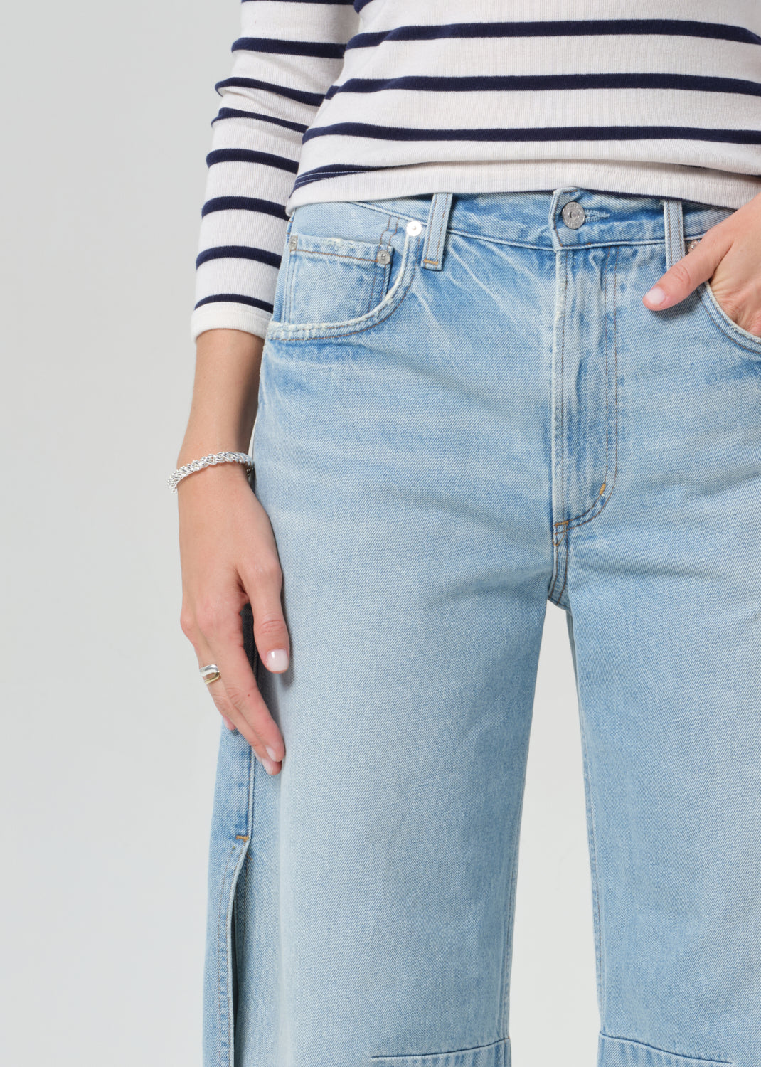 Person wearing a navy and white striped shirt and light blue wide-leg jeans on a grey background