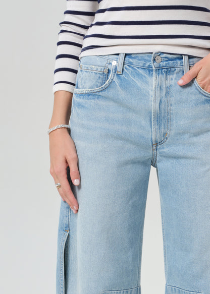 Person wearing a navy and white striped shirt and light blue wide-leg jeans on a grey background