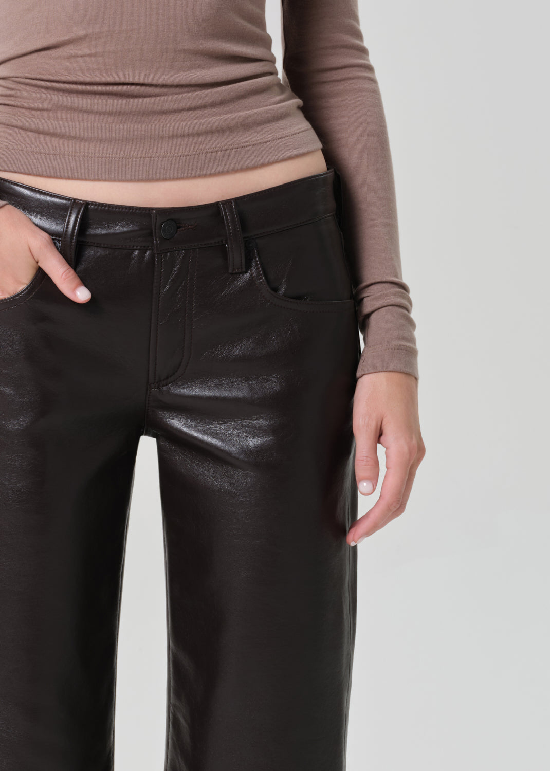 Person wearing a brown turtleneck and dark brown leather pants on a plain background