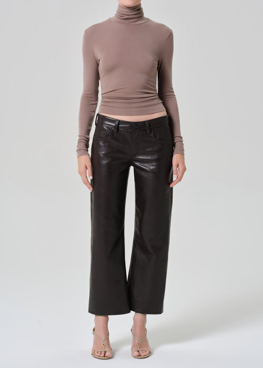 Person wearing a brown turtleneck and dark brown leather pants on a plain background