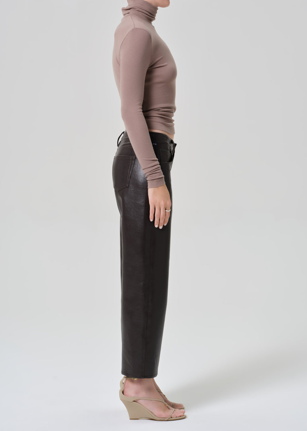 Person wearing a brown turtleneck and dark brown leather pants on a plain background