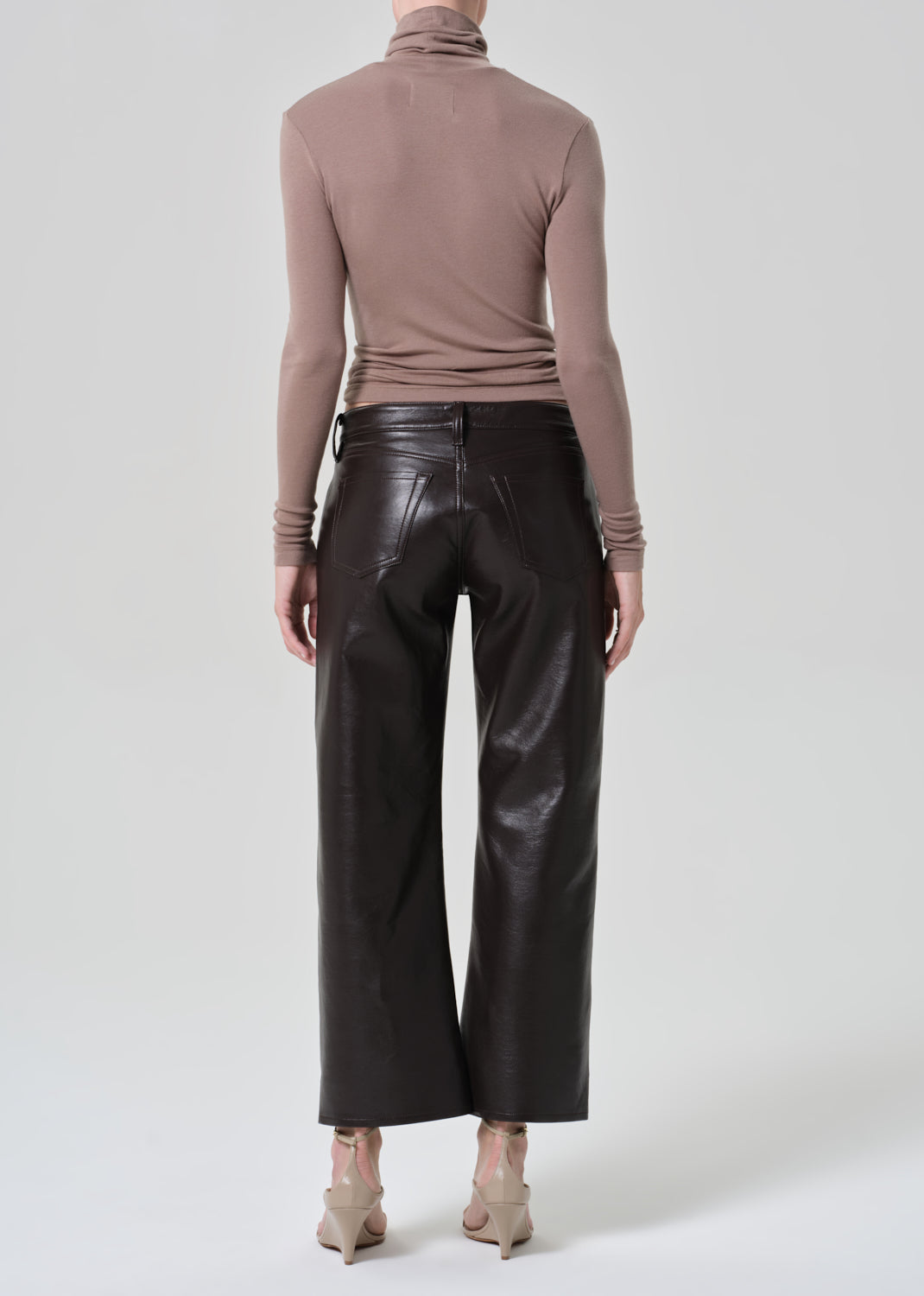 Person wearing a brown turtleneck and dark brown leather pants on a plain background