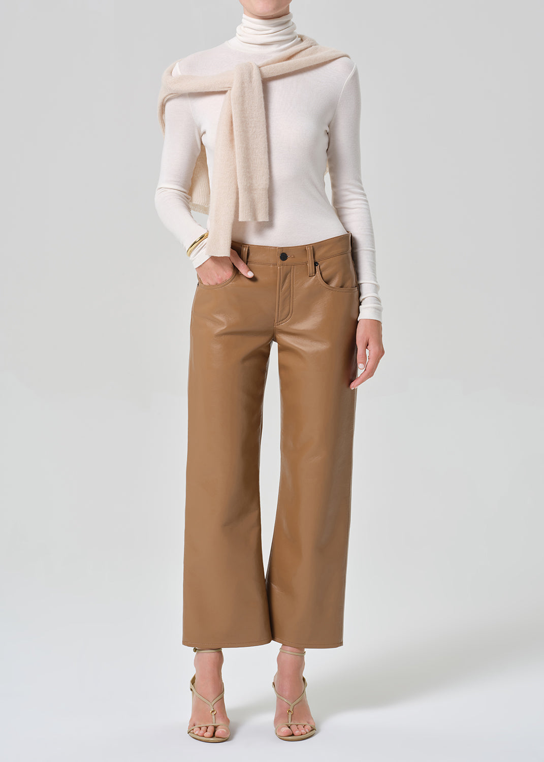 Person wearing a white turtleneck, beige sweater, and tan wide-leg leather pants on a grey background