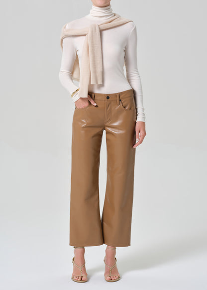Person wearing a white turtleneck and tan leather pants on a light gray background