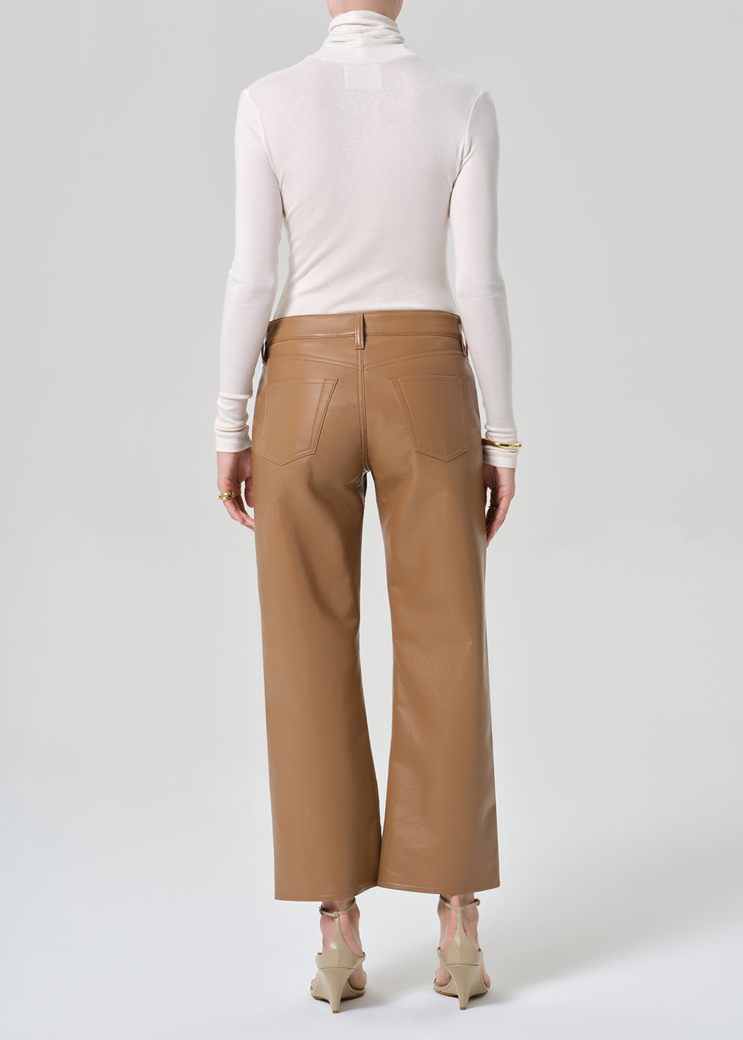 Person wearing a white turtleneck, beige sweater, and tan wide-leg leather pants on a grey background