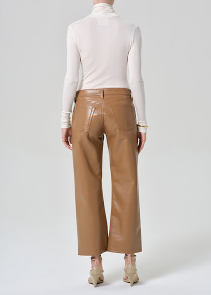Person wearing a white turtleneck and tan leather pants on a light gray background