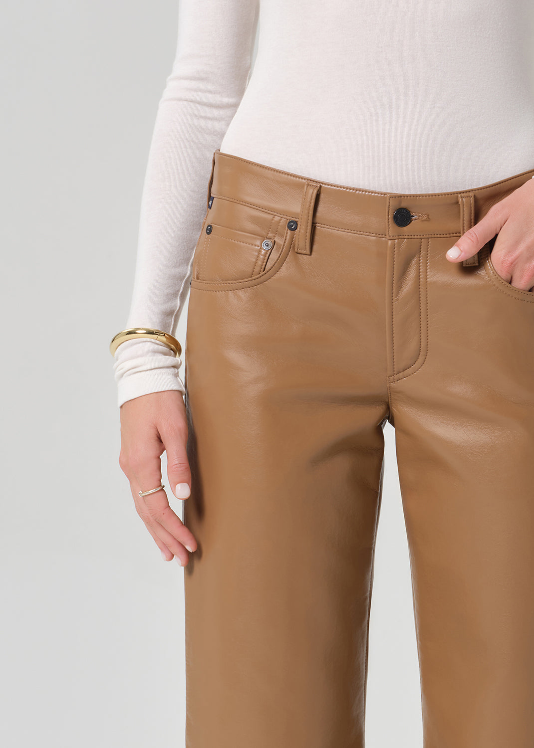 Person wearing a white turtleneck, beige sweater, and tan wide-leg leather pants on a grey background
