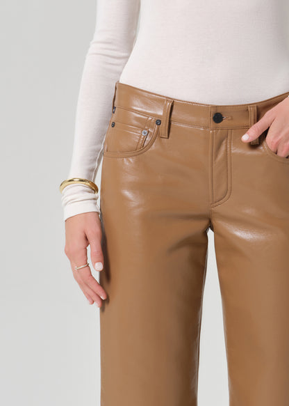 Person wearing a white turtleneck and tan leather pants on a light gray background
