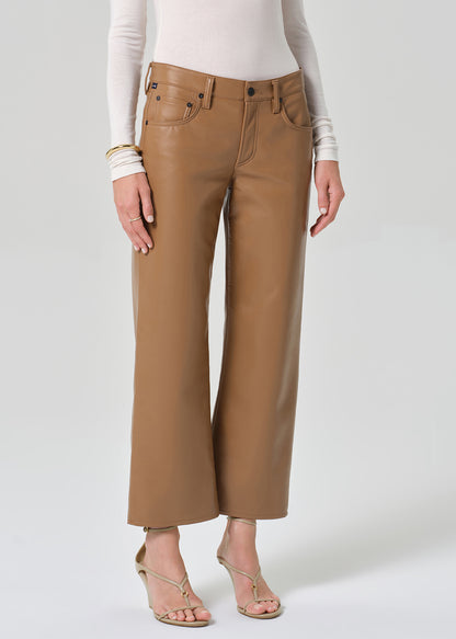 Person wearing a white turtleneck, beige sweater, and tan wide-leg leather pants on a grey background