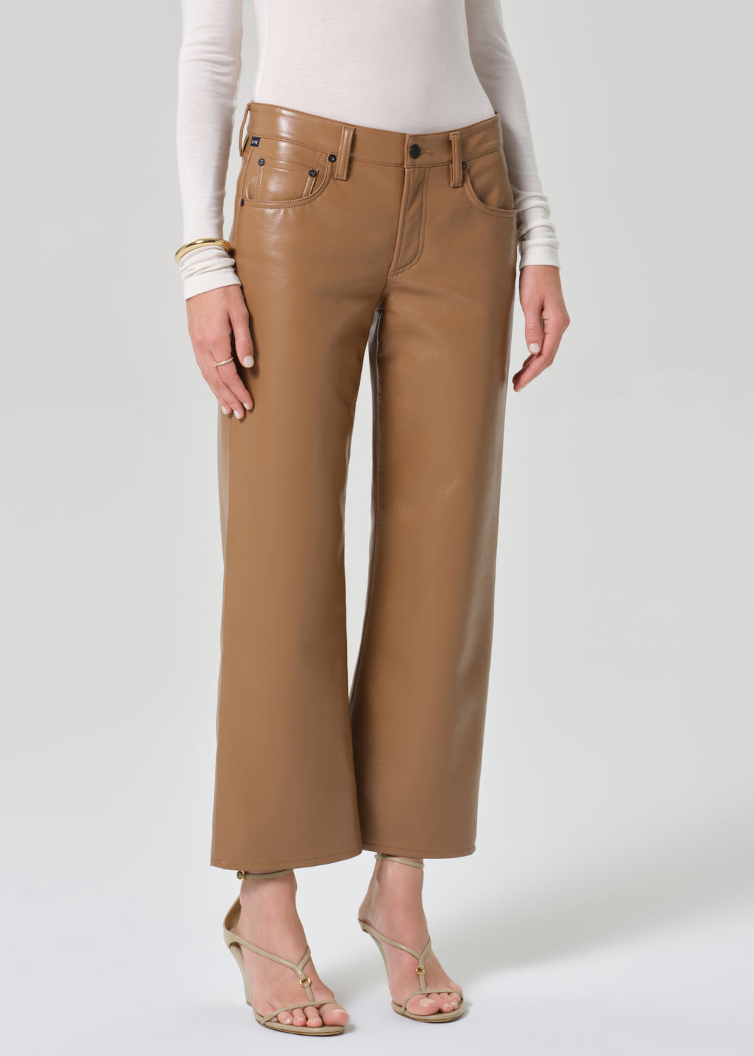 Person wearing a white turtleneck and tan leather pants on a light gray background