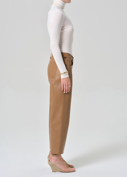Person wearing a white turtleneck, beige sweater, and tan wide-leg leather pants on a grey background