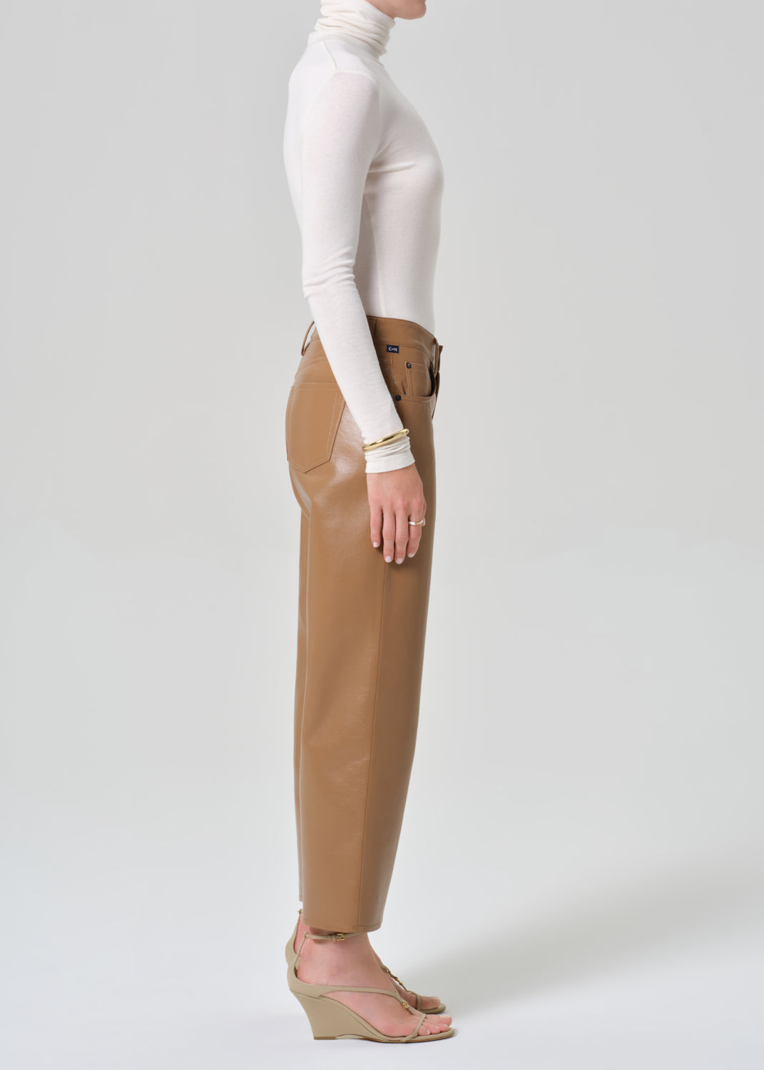 Person wearing a white turtleneck and tan leather pants on a light gray background