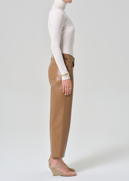 Person wearing a white turtleneck and tan leather pants on a light gray background