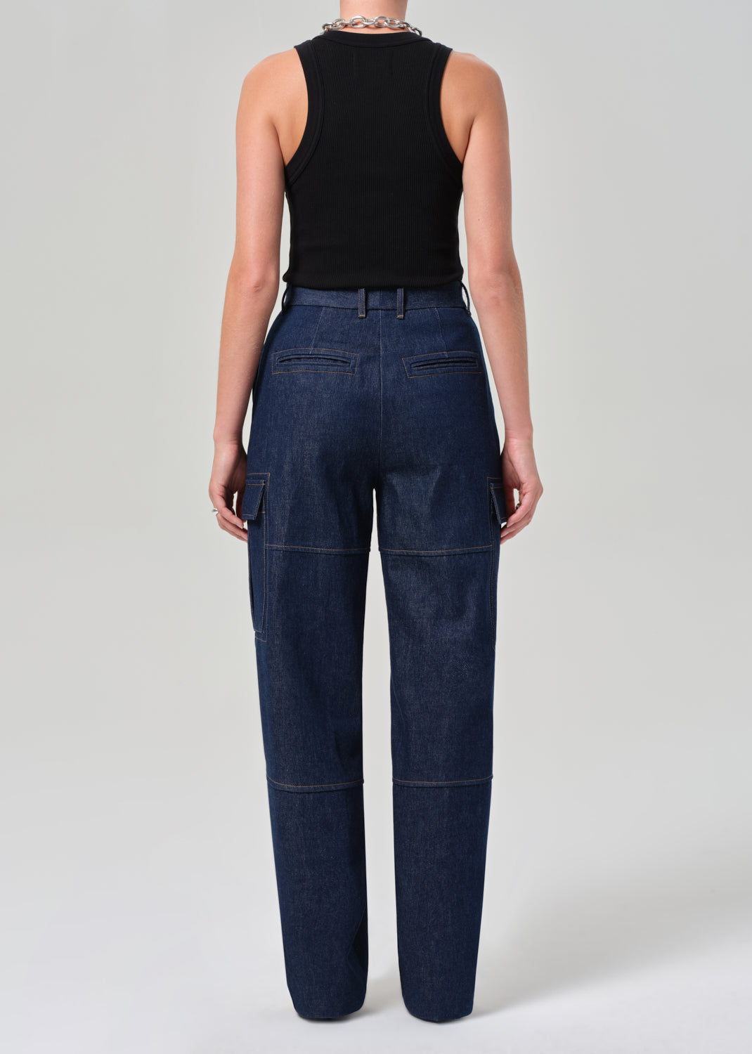 Person wearing dark blue jeans and a black sleeveless top on a light gray background