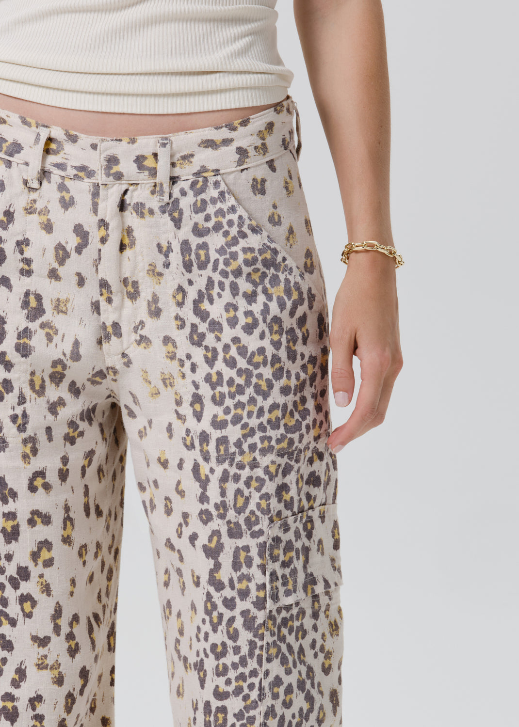 Close-up of a person wearing leopard-print pants with a cream ribbed top, showing the side pocket and hand against a grey background.