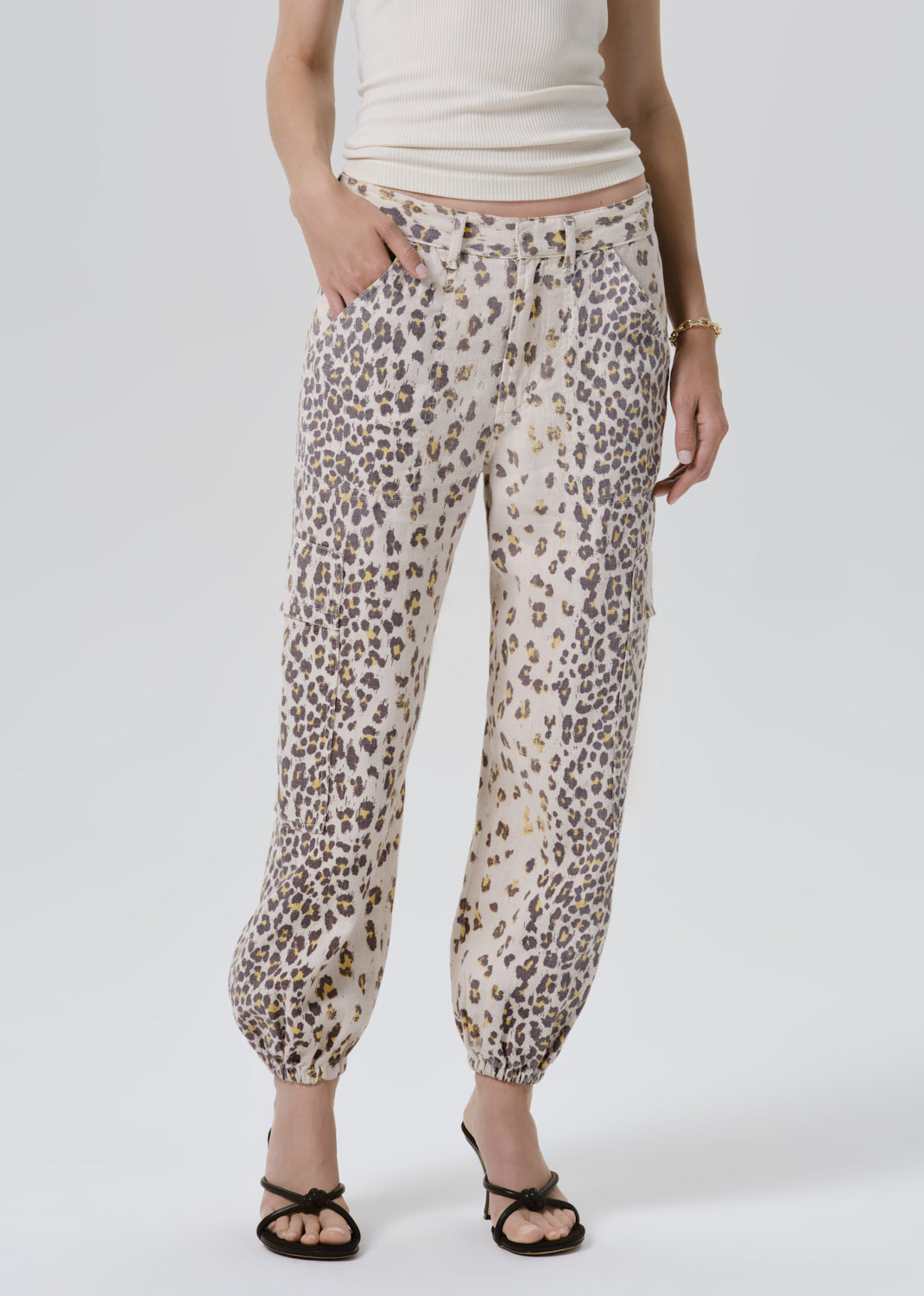 A model wearing beige and brown leopard-print pants with a cream top and black sandals, shown from the waist down against a grey background.