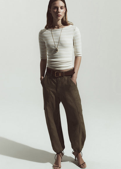 Woman wearing a white top with stripes and brown pants on a plain background