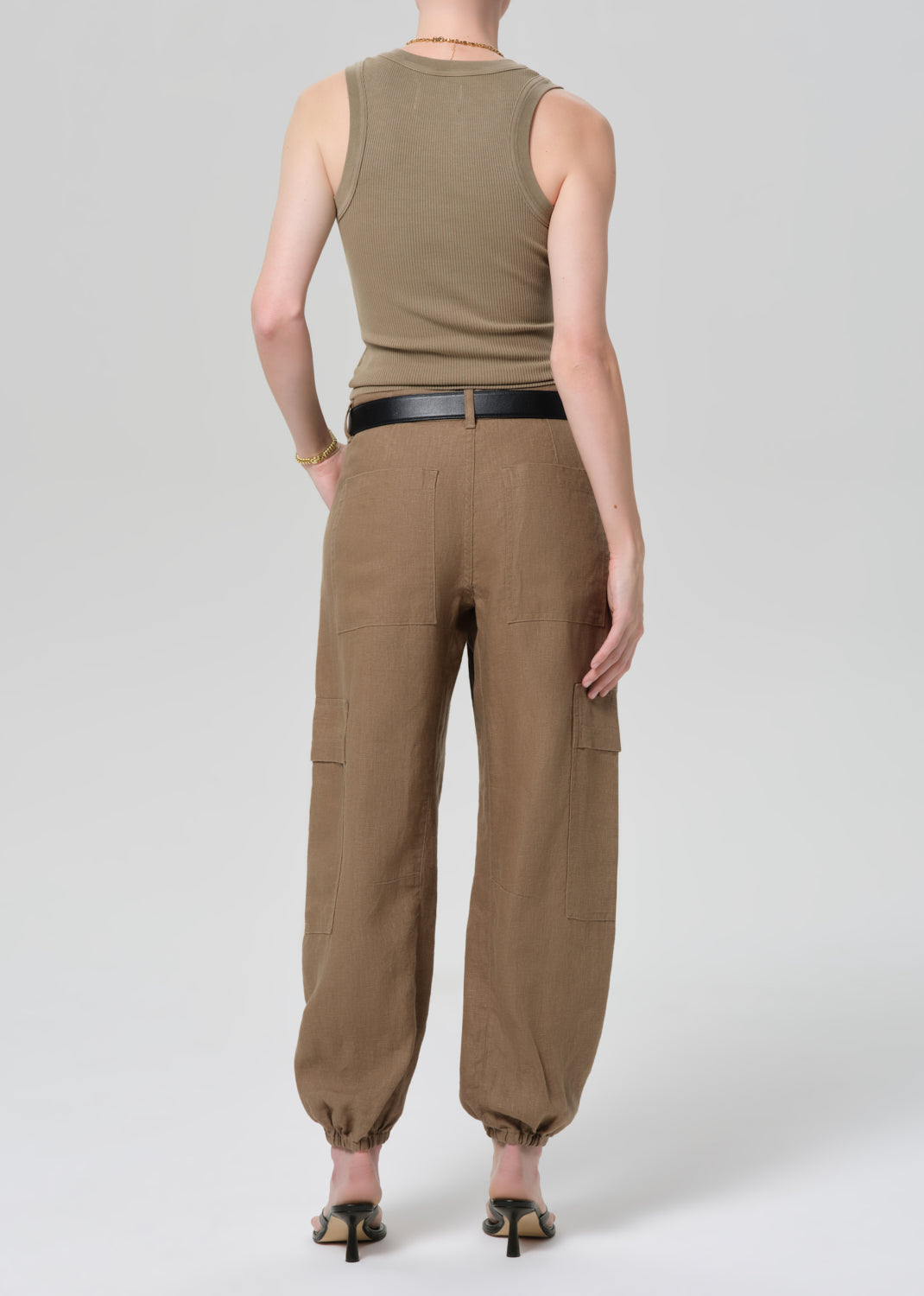 Person wearing a sleeveless olive green top and brown cargo pants on a plain background