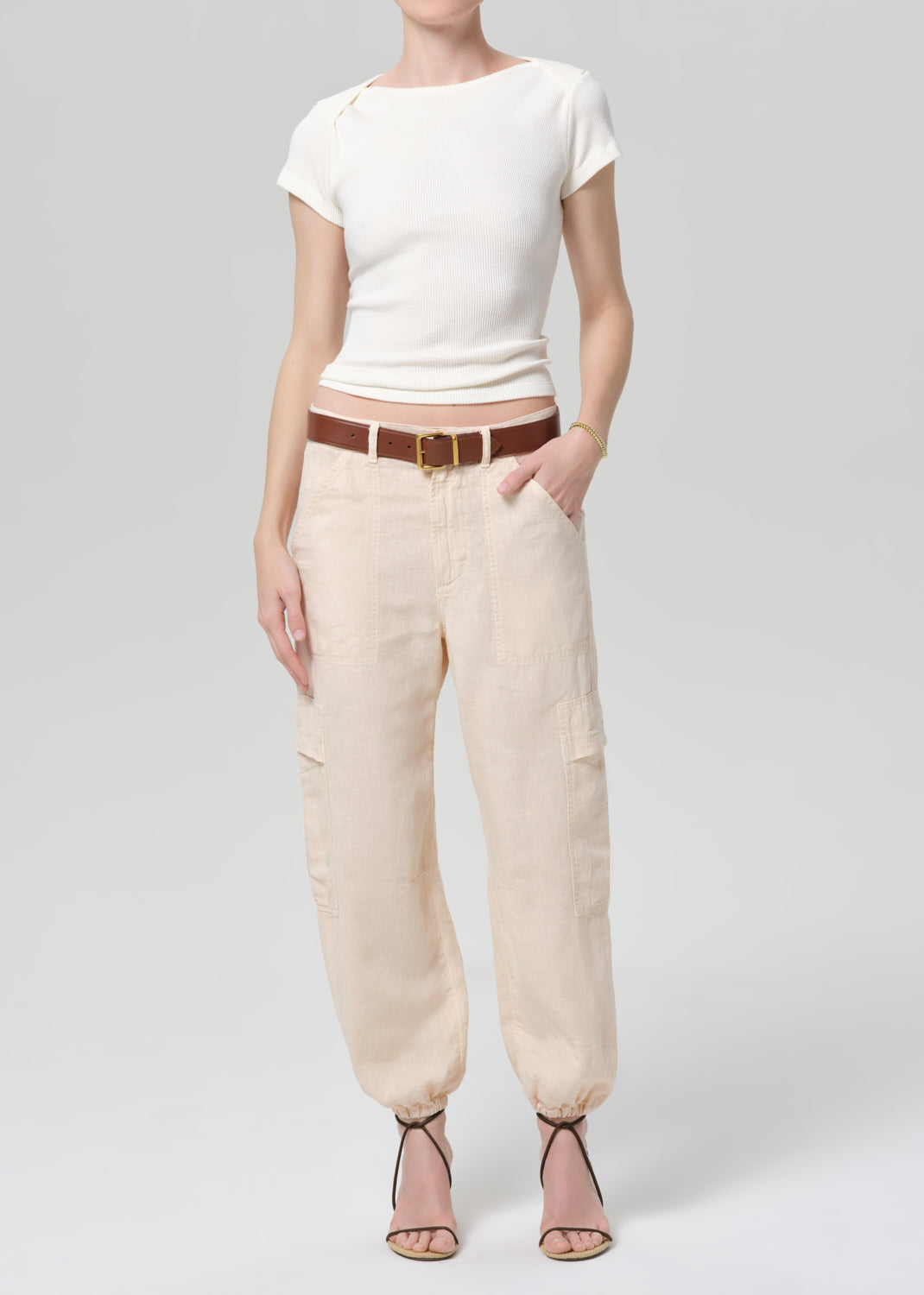Person wearing a white top and beige pants with a brown belt on a light gray background