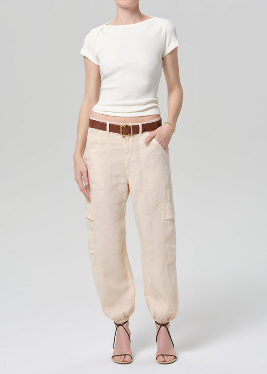 Person wearing a white top and beige pants with a brown belt on a light gray background