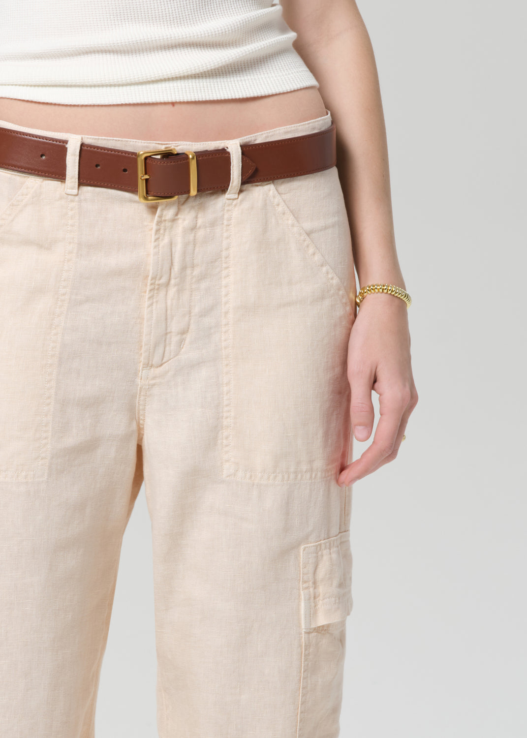 Person wearing beige cargo pants with a brown belt on a light gray background