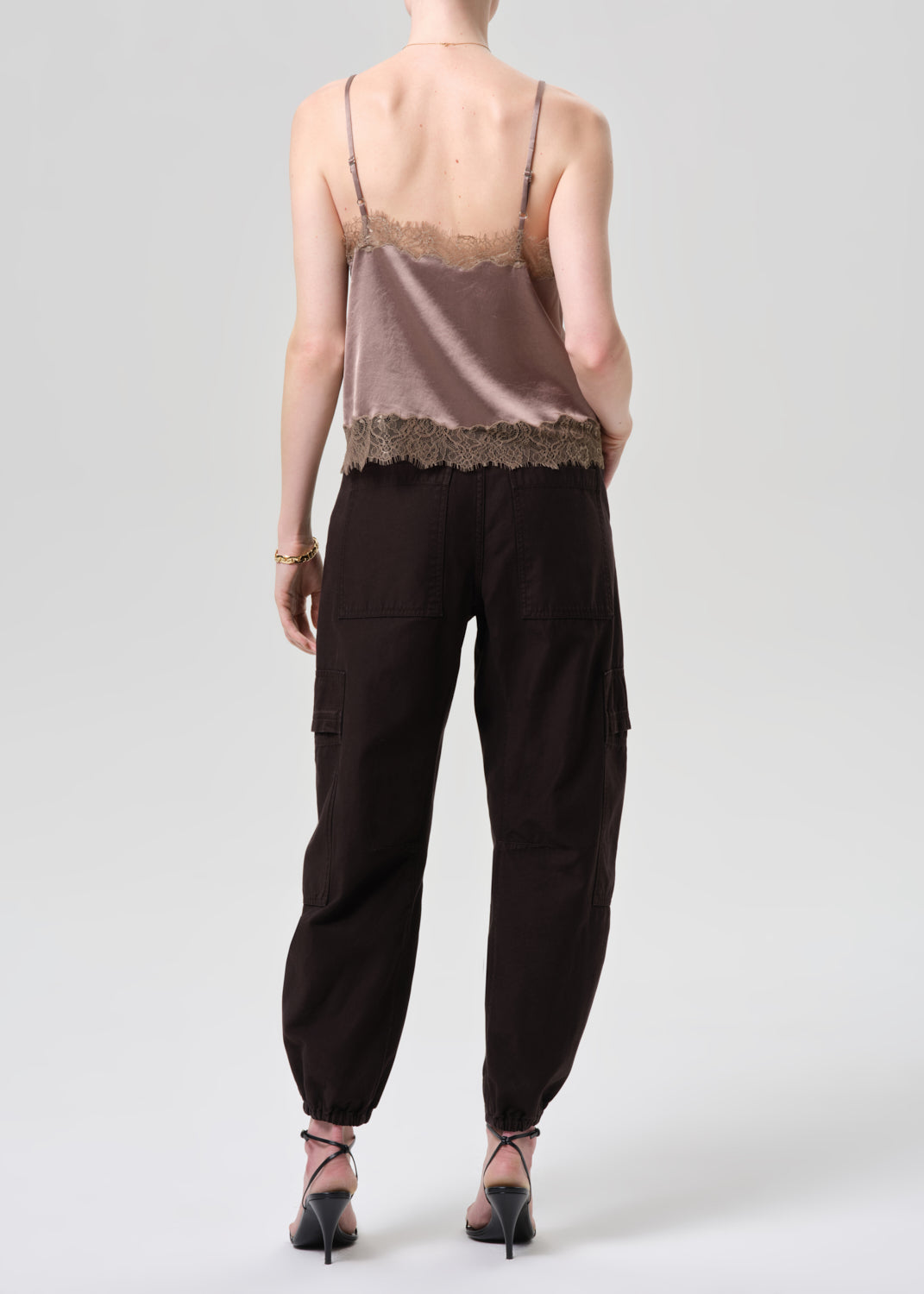 Person wearing a beige lace top and black cargo pants on a grey background
