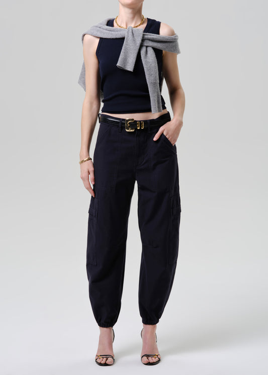 Person wearing a black sleeveless top, black pants, and a grey scarf on a grey background