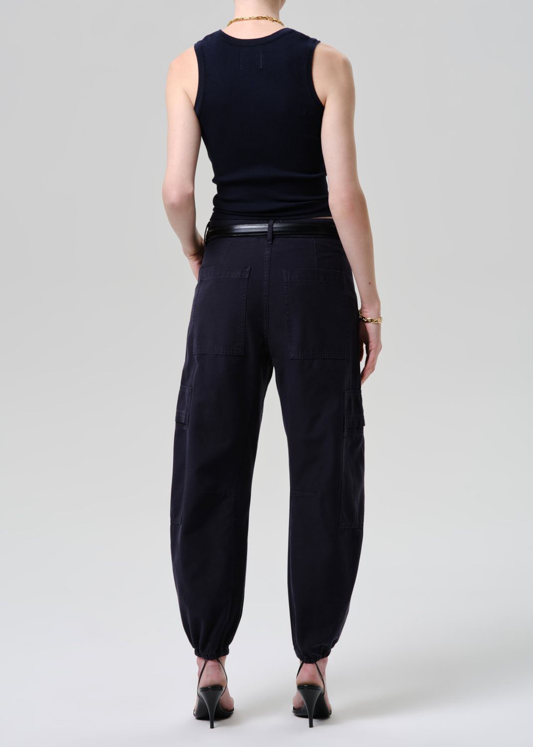 Person wearing a black sleeveless top and black pants on a grey background