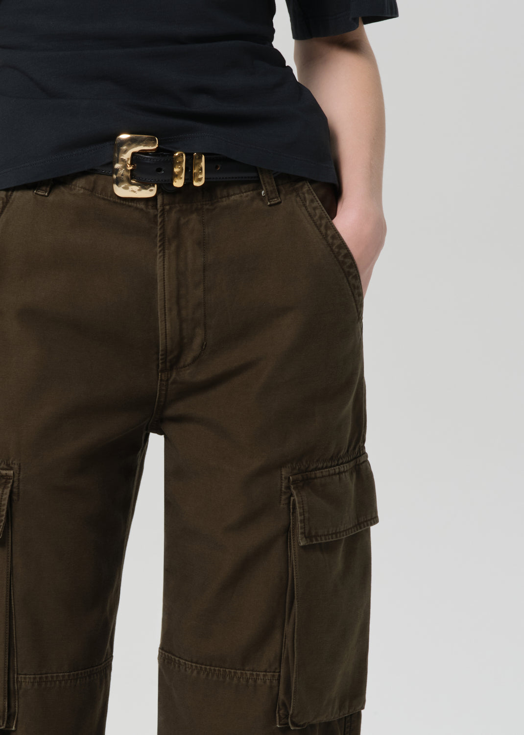 Person wearing a black t-shirt and green cargo pants on a light gray background