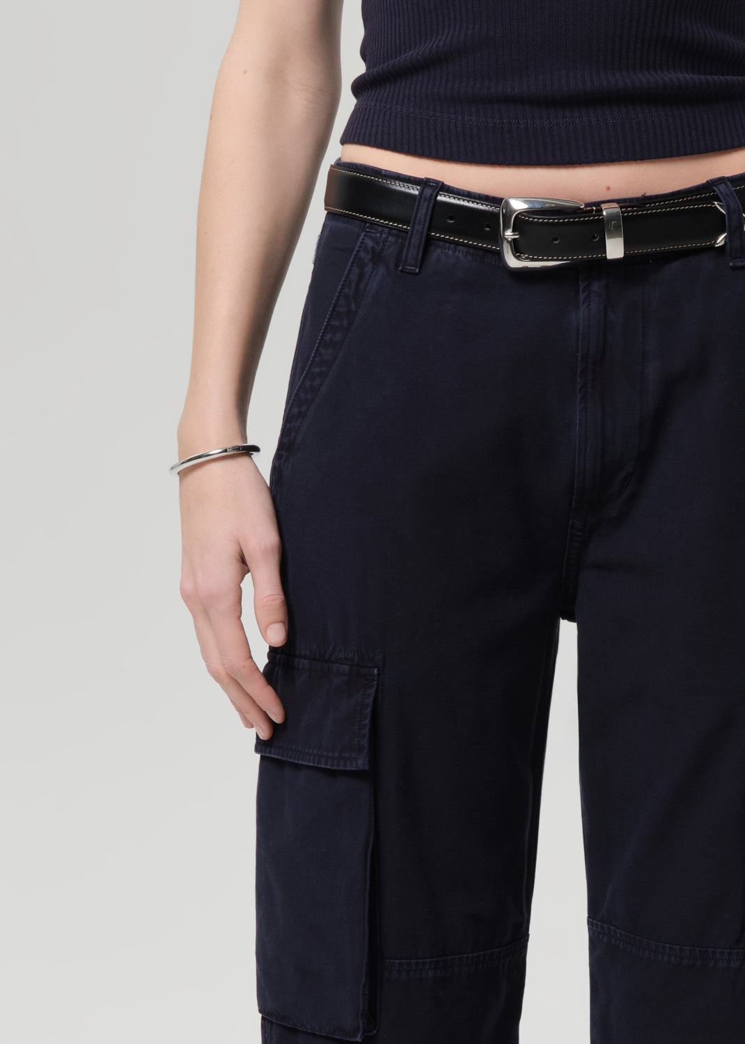 Person wearing a navy tee and navy cargo pants with a belt on a grey background