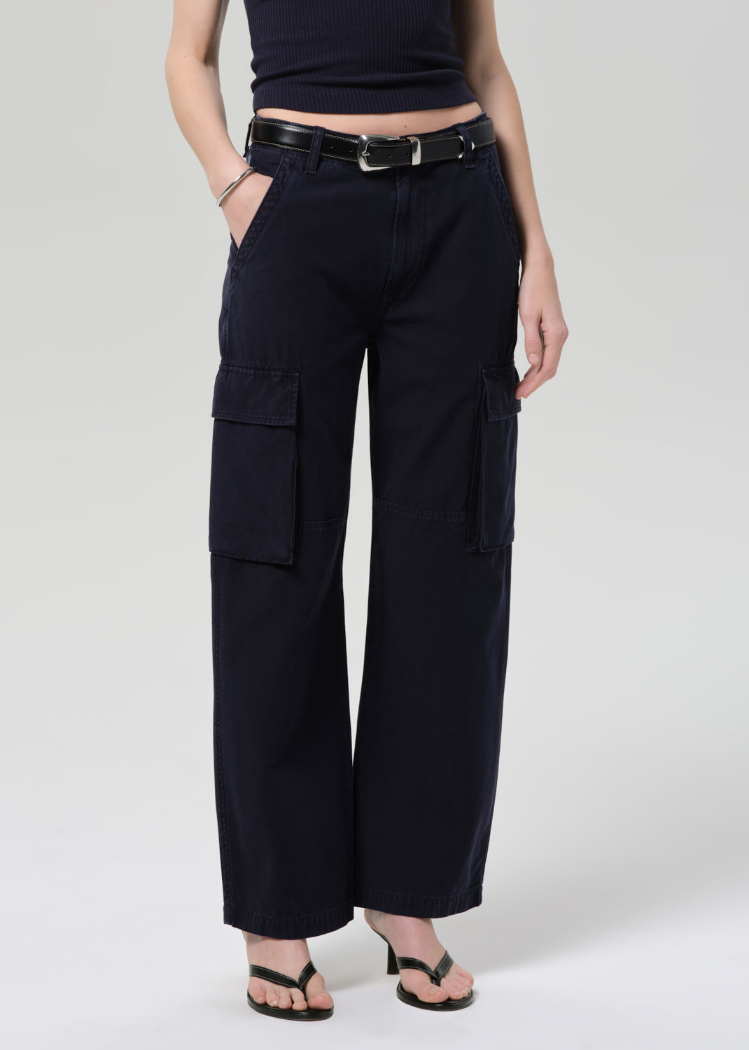 Person wearing a navy tee and navy cargo pants with a belt on a grey background