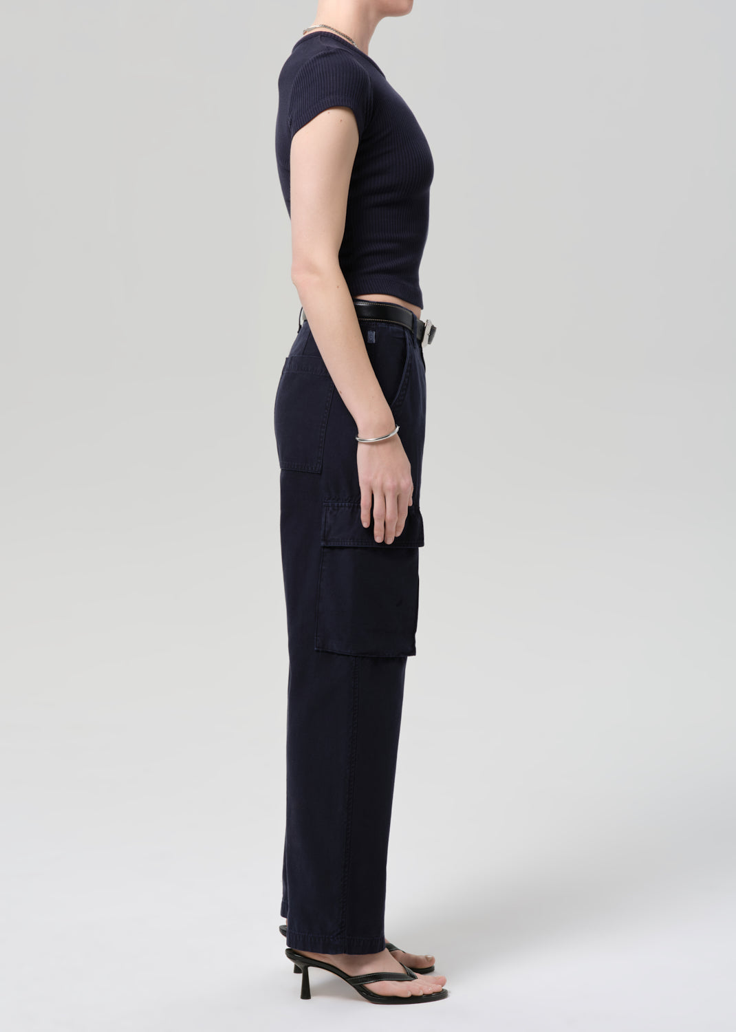 Person wearing a navy tee and navy cargo pants with a belt on a grey background