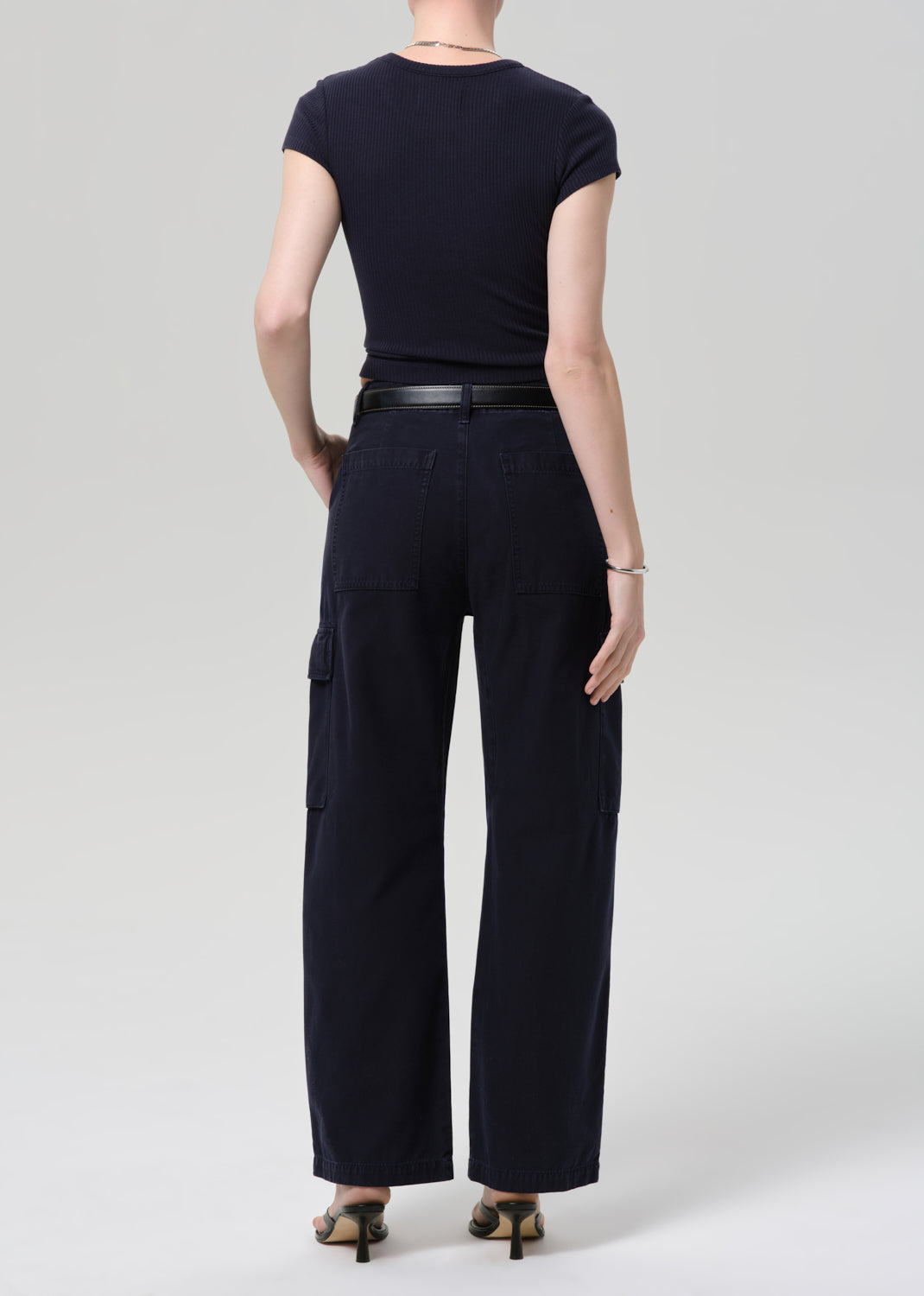 Person wearing a navy tee and navy cargo pants with a belt on a grey background