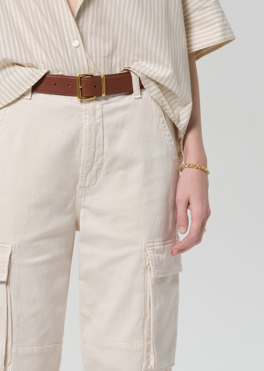 Person wearing beige cargo pants with a brown belt on a grey background
