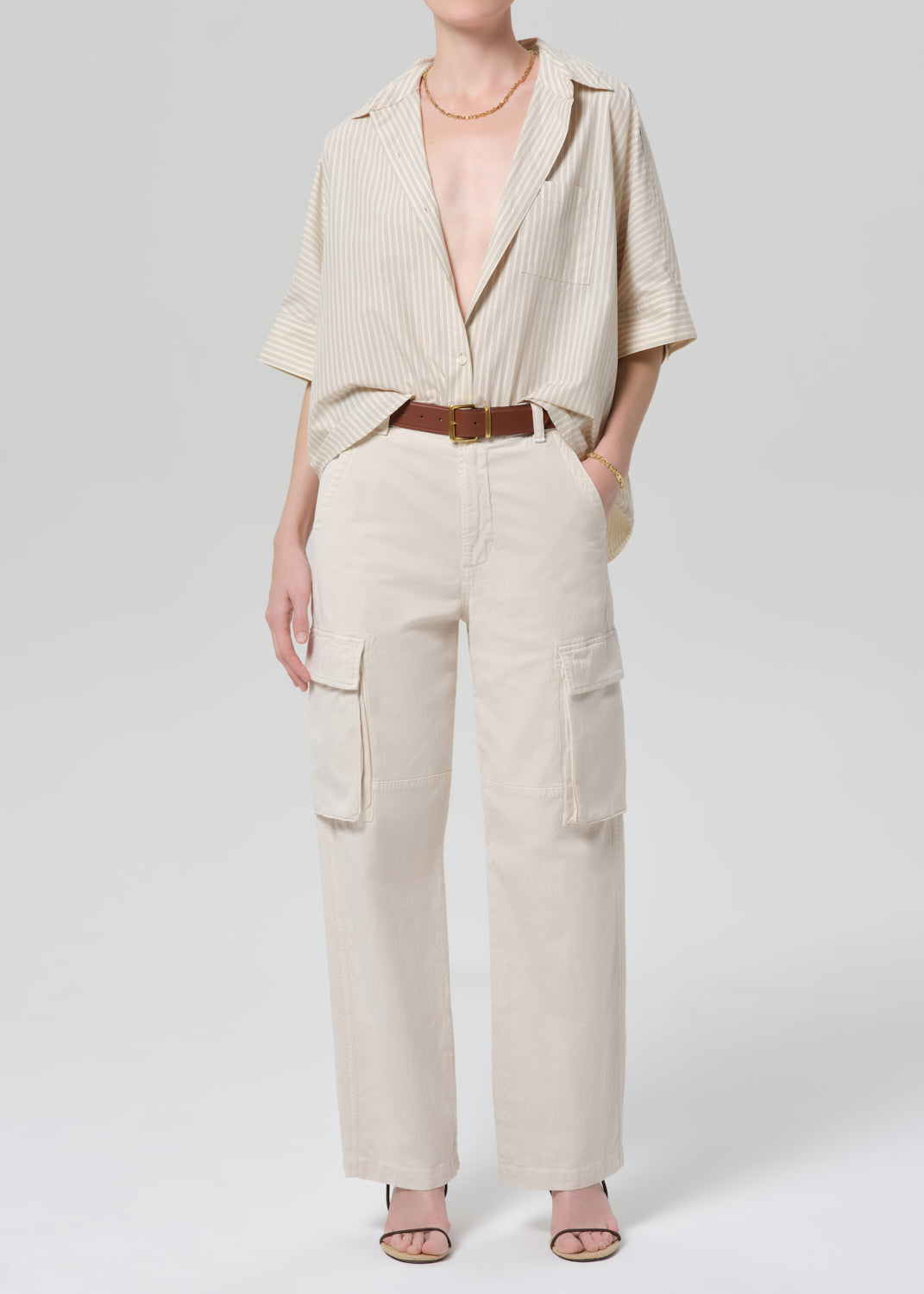 Person wearing a beige outfit with a belt on a grey background