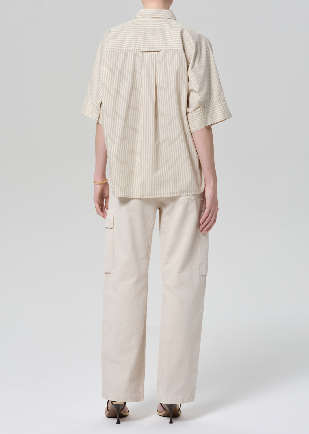 Person wearing a beige outfit with a shirt and pants on a grey background