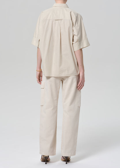 Person wearing a beige outfit with a shirt and pants on a grey background