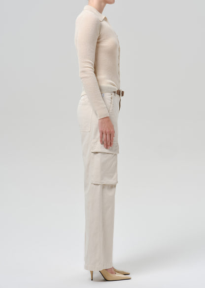 A model shown in profile wearing a cream-colored long-sleeve knit top and matching high-waisted cargo pants with a brown belt, paired with beige pointed-toe heels, against a grey background.