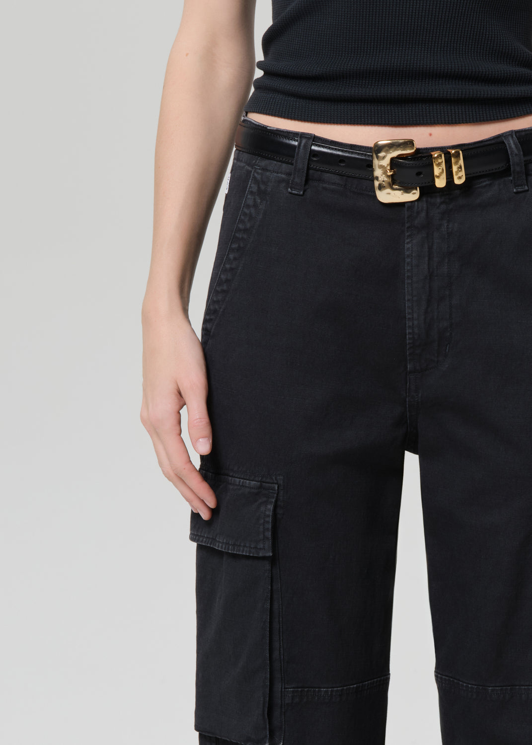 Person wearing a black tee with black cargo pants and a belt on a grey background