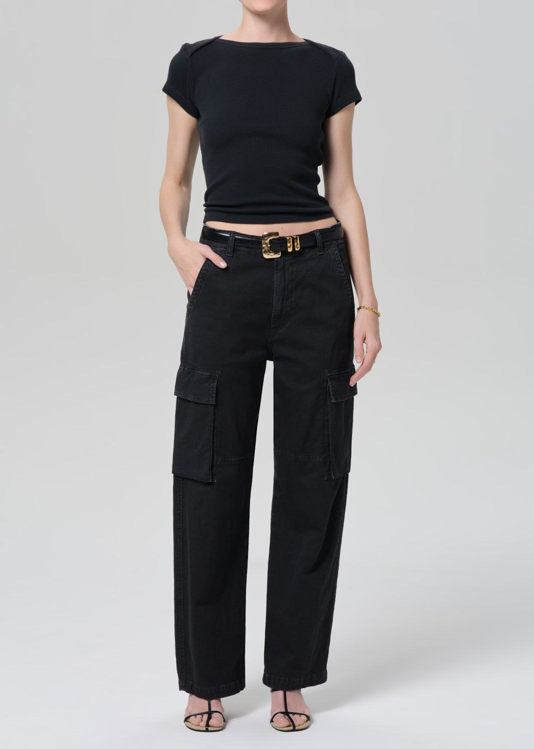 Person wearing a black tee with black cargo pants and a belt on a grey background