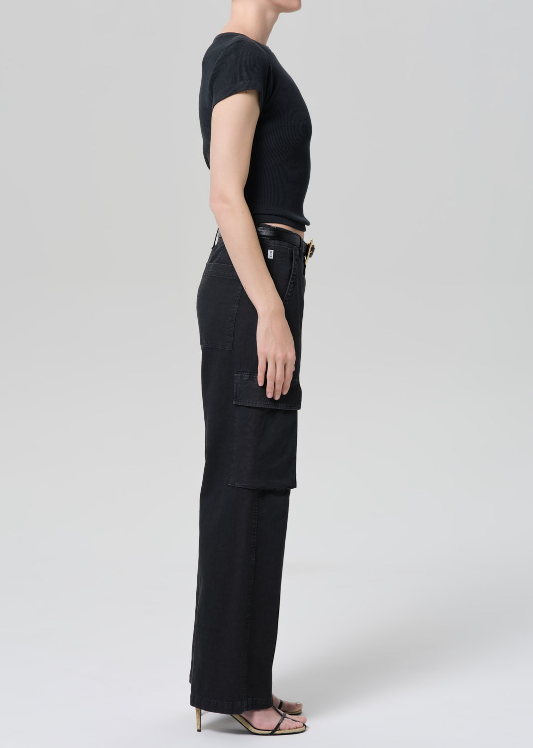 Person wearing a black tee with black cargo pants and a belt on a grey background