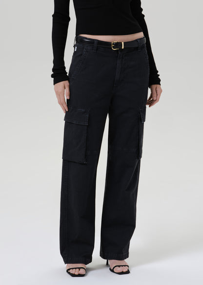 A model wearing black wide-leg cargo pants with a black belt, styled with a black long-sleeve top and black heeled sandals against a grey background.