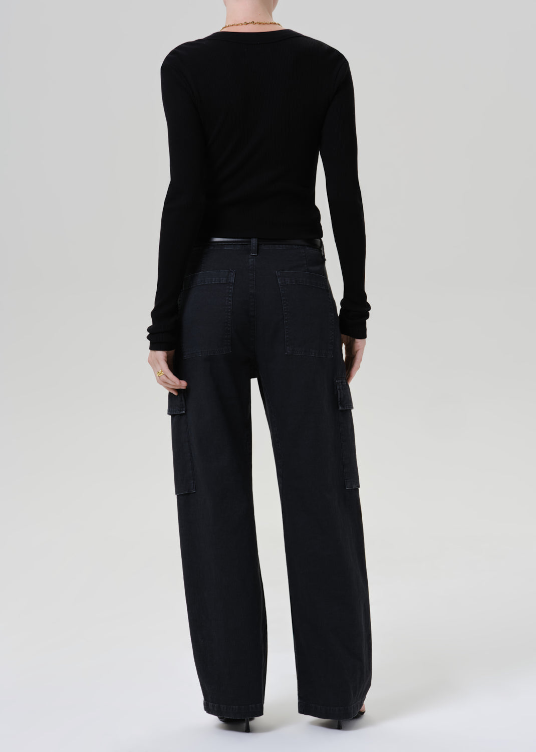 A model shown from the back wearing a black long-sleeve top and black wide-leg cargo pants against a grey background.