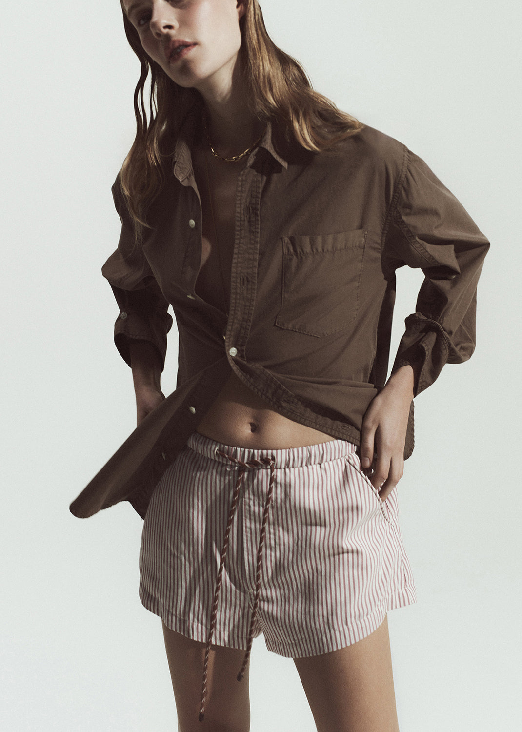 Woman wearing a brown shirt and striped shorts on a plain background
