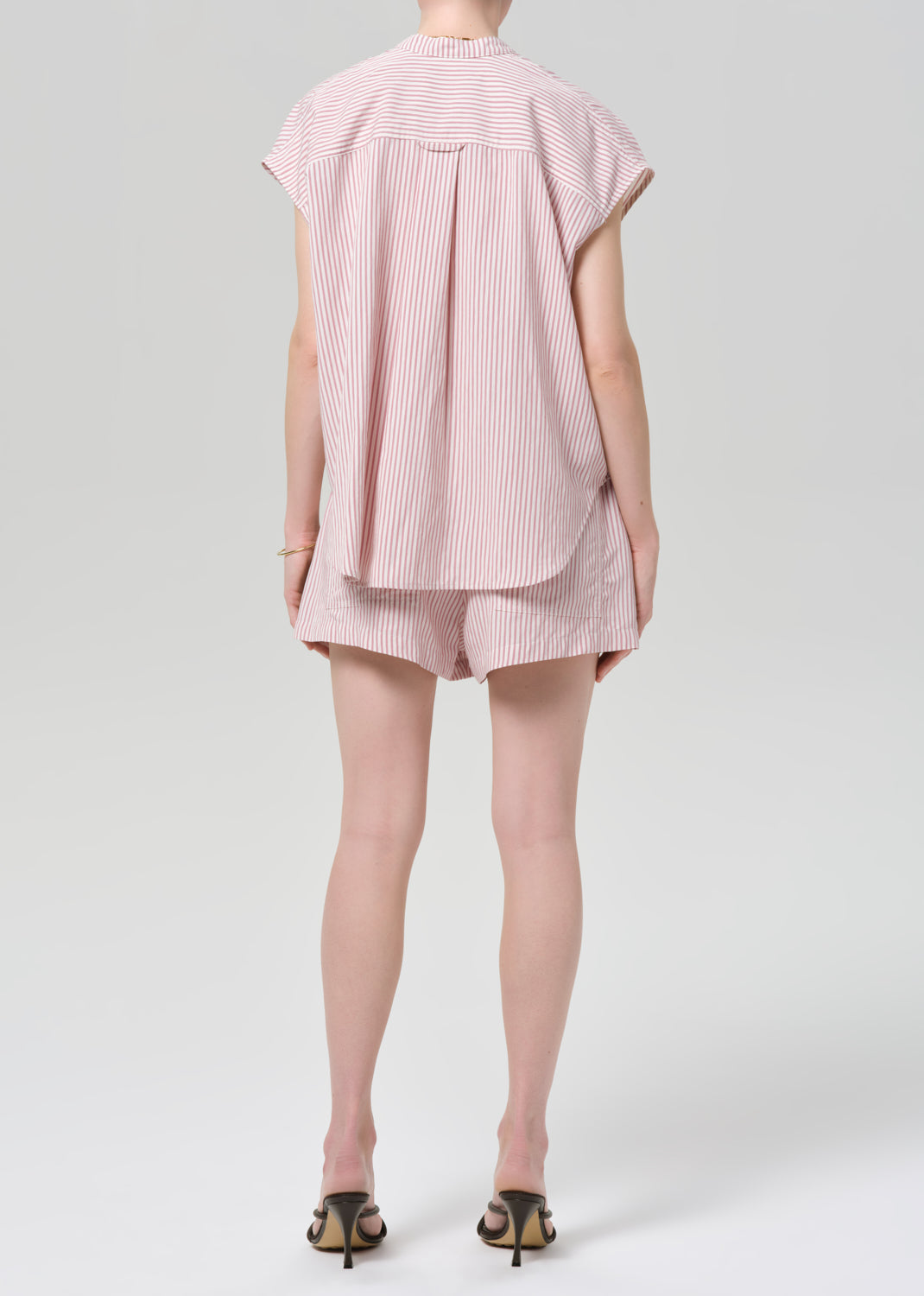 Person wearing a pink striped shirt with matching shorts on a grey background